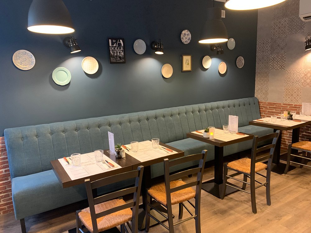 Salle intérieure : banquette capitonnée, tables en bois et suspensions dorées.