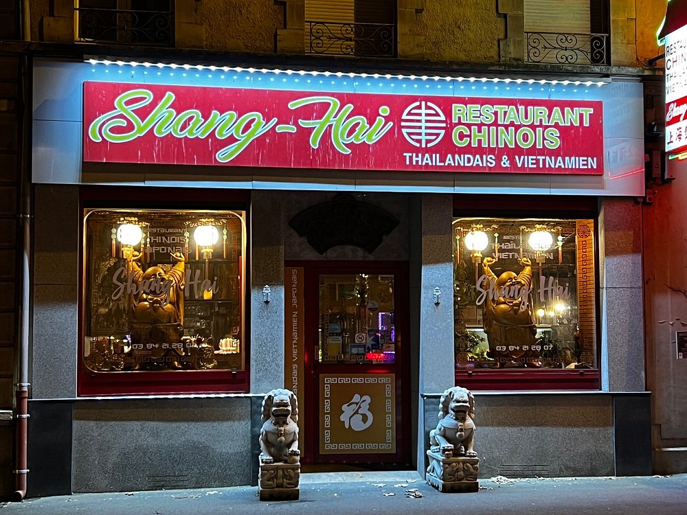 Façade illuminée du restaurant Shang'Hai la nuit : enseigne rouge, lions gardiens en pierre et lanternes.