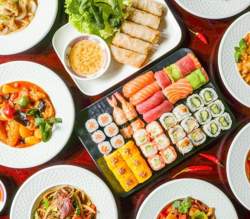 Grande tablée de plats asiatiques : plateau de sushis et makis, nems, currys, plats sautés sur table laquée rouge.