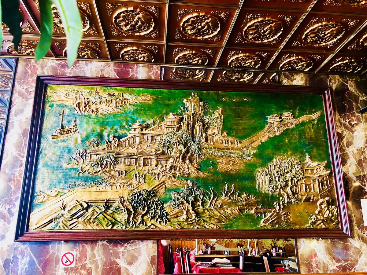 Fresque sculptée représentant un paysage chinois en jade et or, sous le plafond doré du restaurant.